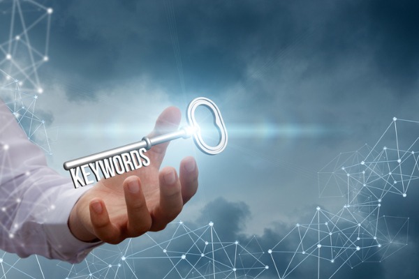 An image showing a person holding a silver key with the teeth of the key spelling out “keywords.”