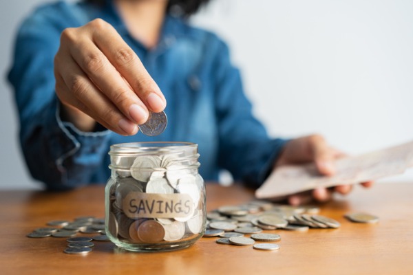 An image showing someone saving money in a jar.