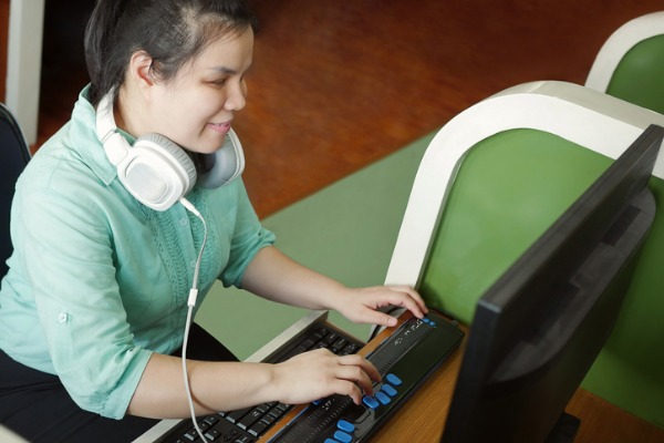 Young blind woman with headphones using compute