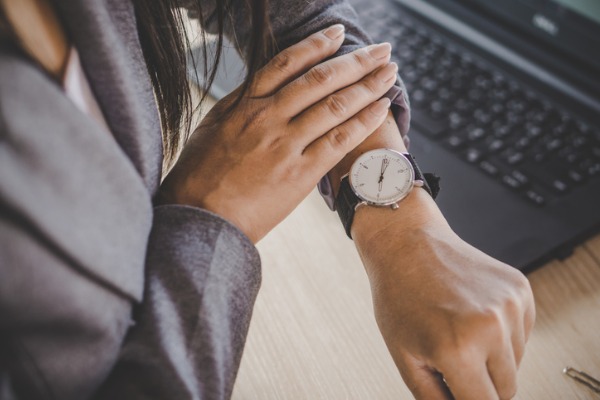 An image showing a person looking at their watch next to a computer. 