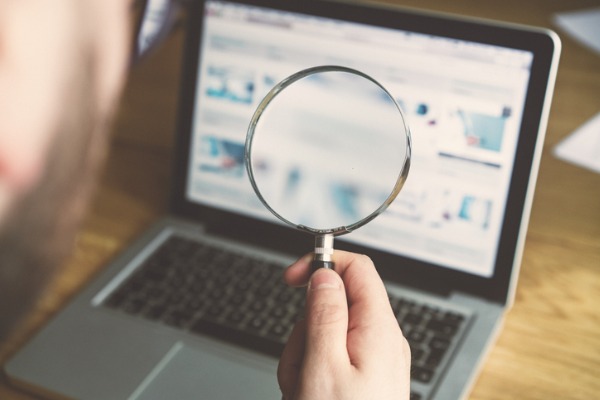 An image of a magnifying glass being held up to a laptop to show finding keywords for voice search. 