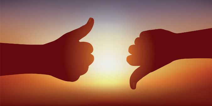 An image showing a person holding a thumbs up and a person holding a thumbs down in front of a setting sun. 